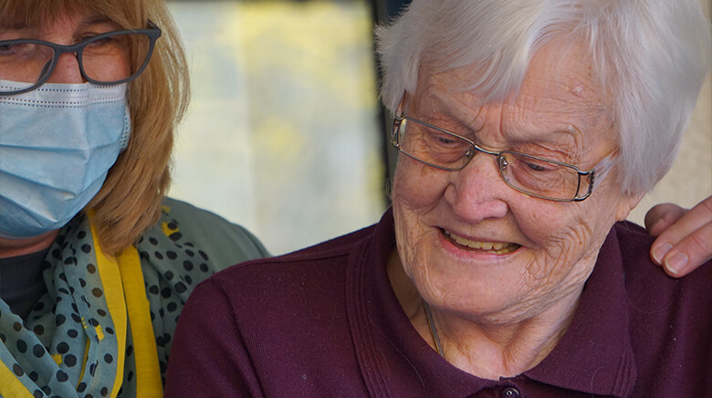 Elderly woman with white hair and glasses, smiling gently.