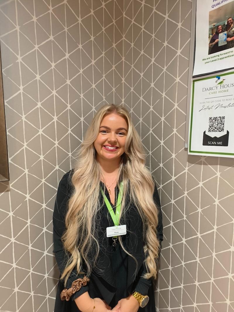 woman with long blonde hair wearing a black cardigan and green lanyard having a headshot taken for the team page