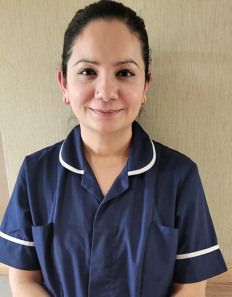 woman with brown hair tied back and wearing a blue nursing uniform having a headshot taken for the team page