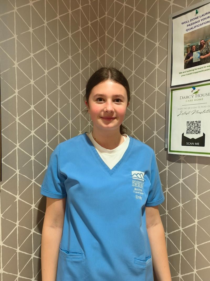 girl with brown hair tied back in a ponytail wearing a blue placement uniform having a headshot taken for the team page