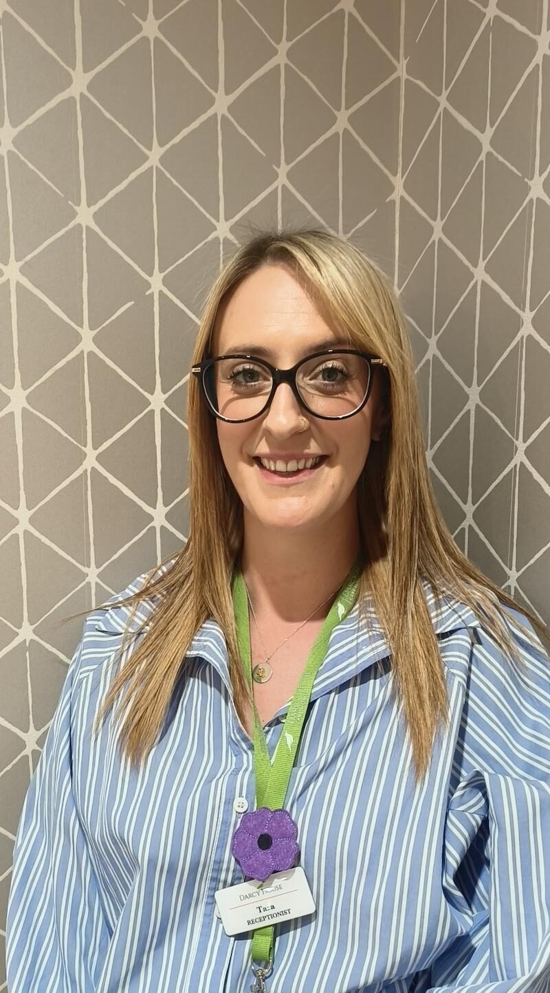 woman with blonde hair wearing a blue stripey shirt and green lanyard having a headshot taken for the team page