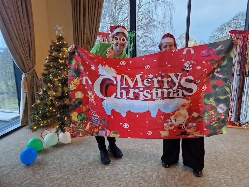 two team members with christmas hats on holding up a sign that says Merry Christmas